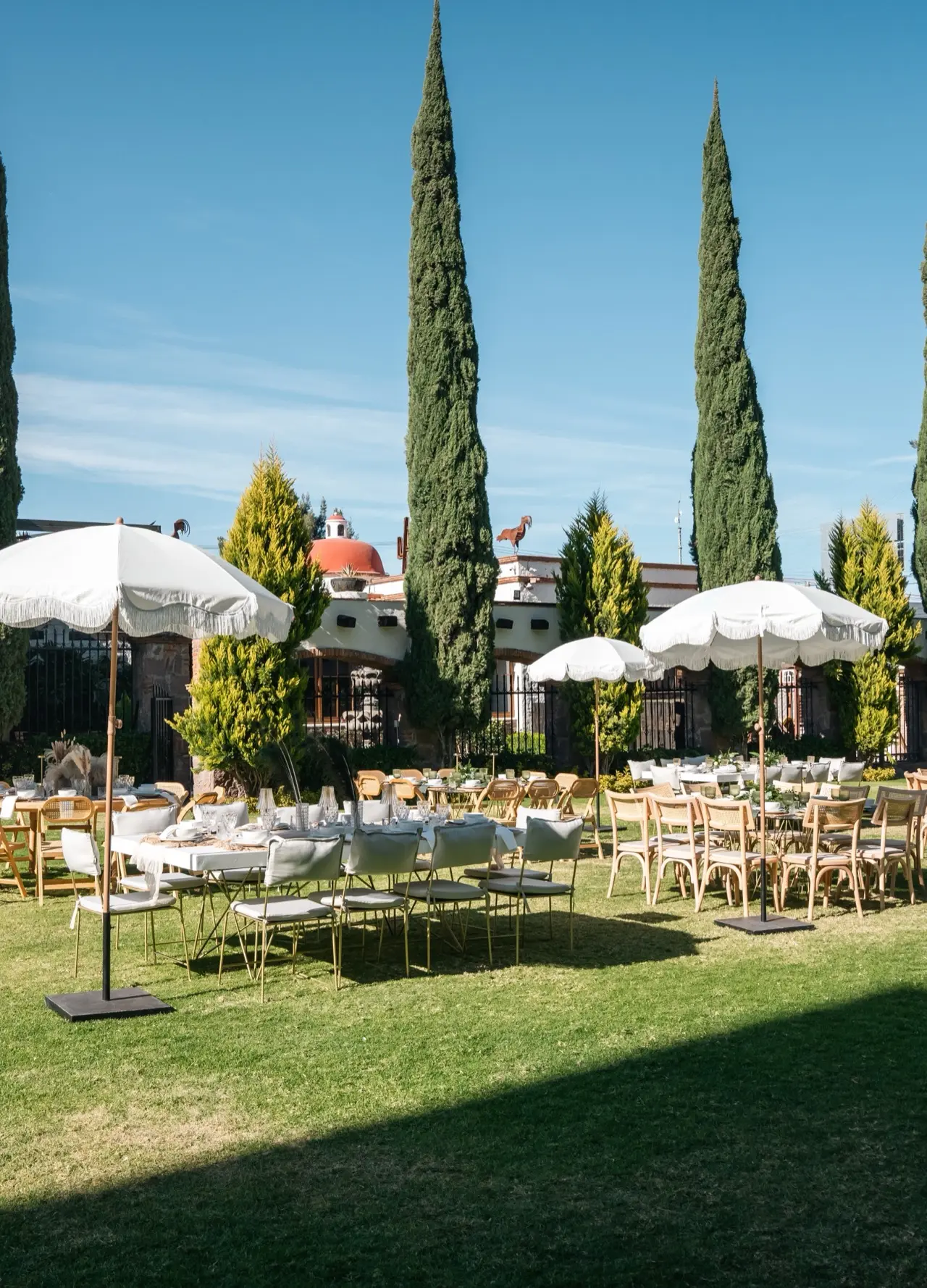 Jard&iacute;n de Hacienda de Piedra con mesas redondas montadas bajo sombrillas blancas